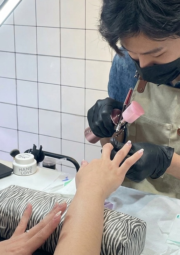 Gros plan extrême montrant une fine brume violette pulvérisée par un aérographe sur le bout dun ongle.