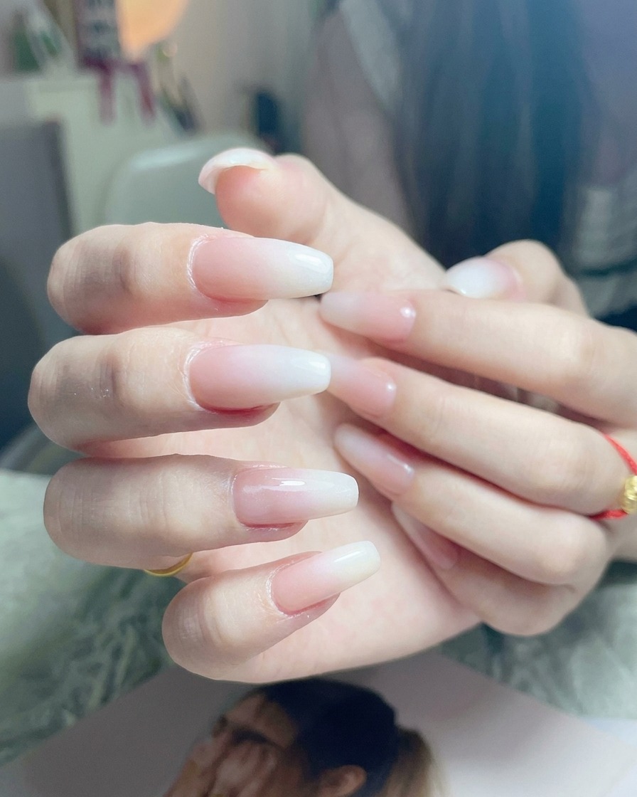 Un pinceau appliquant une couche finale de top coat transparent et brillant sur un ongle ombré blanc terminé.
