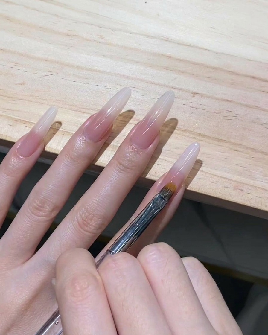 Un pinceau à ombré effilé tirant délicatement du gel blanc laiteux non catalysé vers le bas sur une extension dongle stiletto transparente.