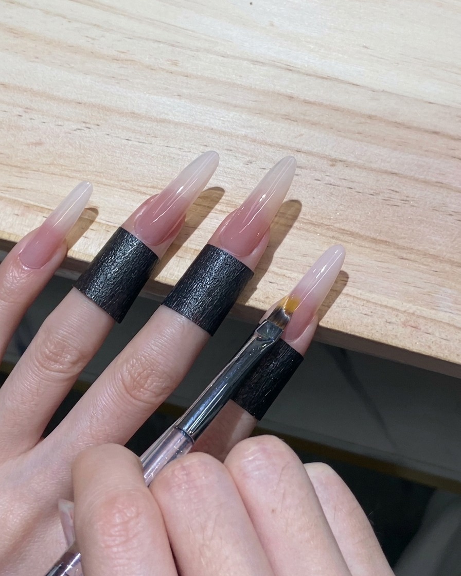 Un pinceau à ombré effectuant de légers balayages pour estomper le bord du gel blanc sur un ongle stiletto.