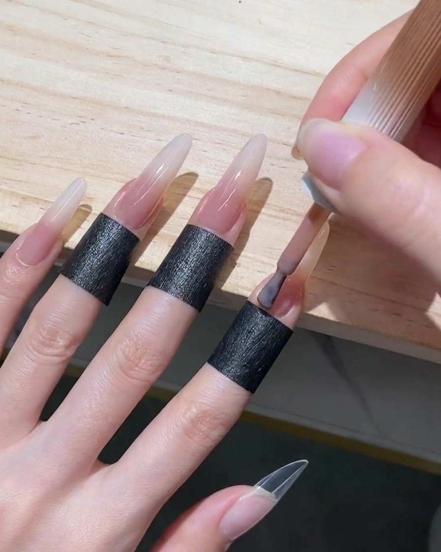 Application dun vernis gel rose nude translucide près des cuticules et sur la moitié inférieure dun long ongle stiletto.