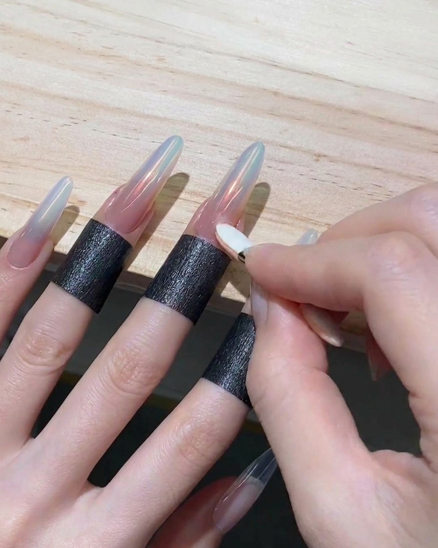 Une main utilisant un petit embout en mousse pour frotter une poudre irisée orange sur la pointe dun ongle long.