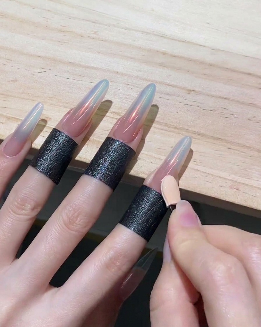 Une main utilisant le côté propre dun applicateur en mousse pour étirer la poudre chrome vers le bas sur un ongle, créant un effet ombré.