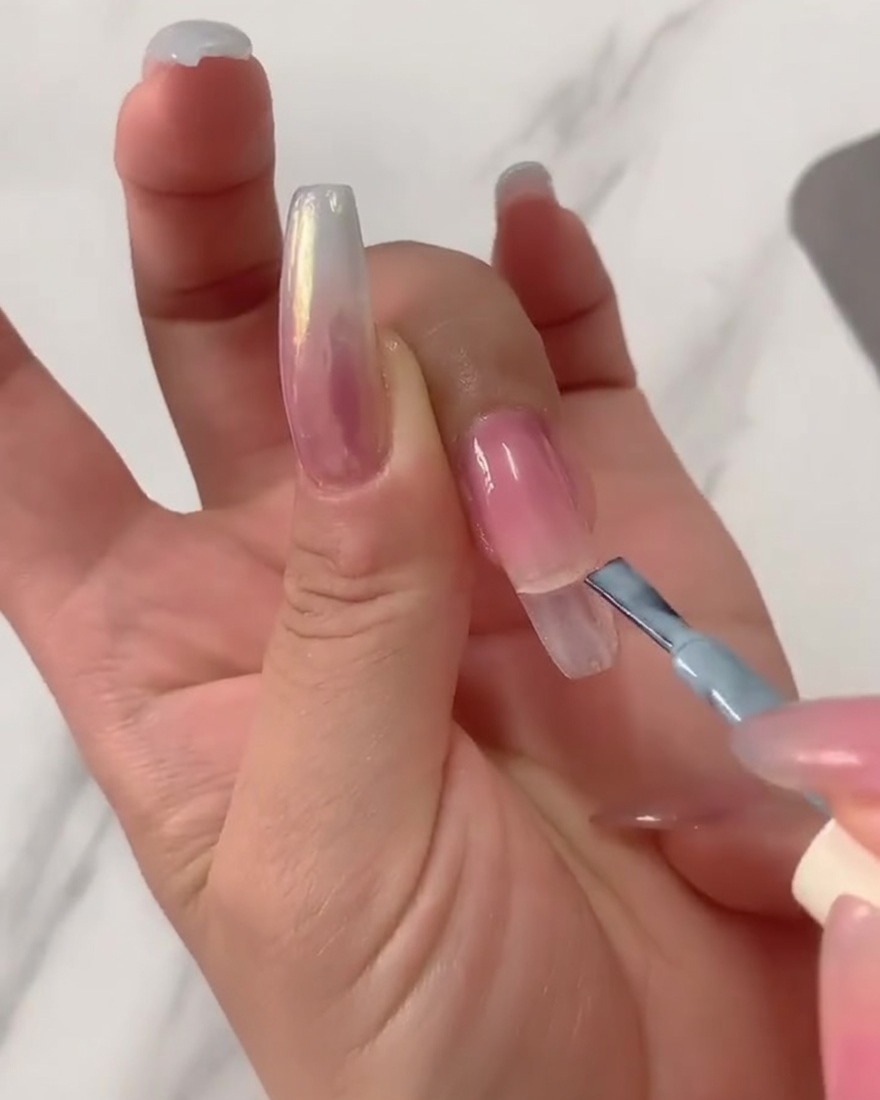 Gros plan dun pinceau appliquant du vernis gel bleu clair sur la moitié supérieure dune longue capsule transparente.