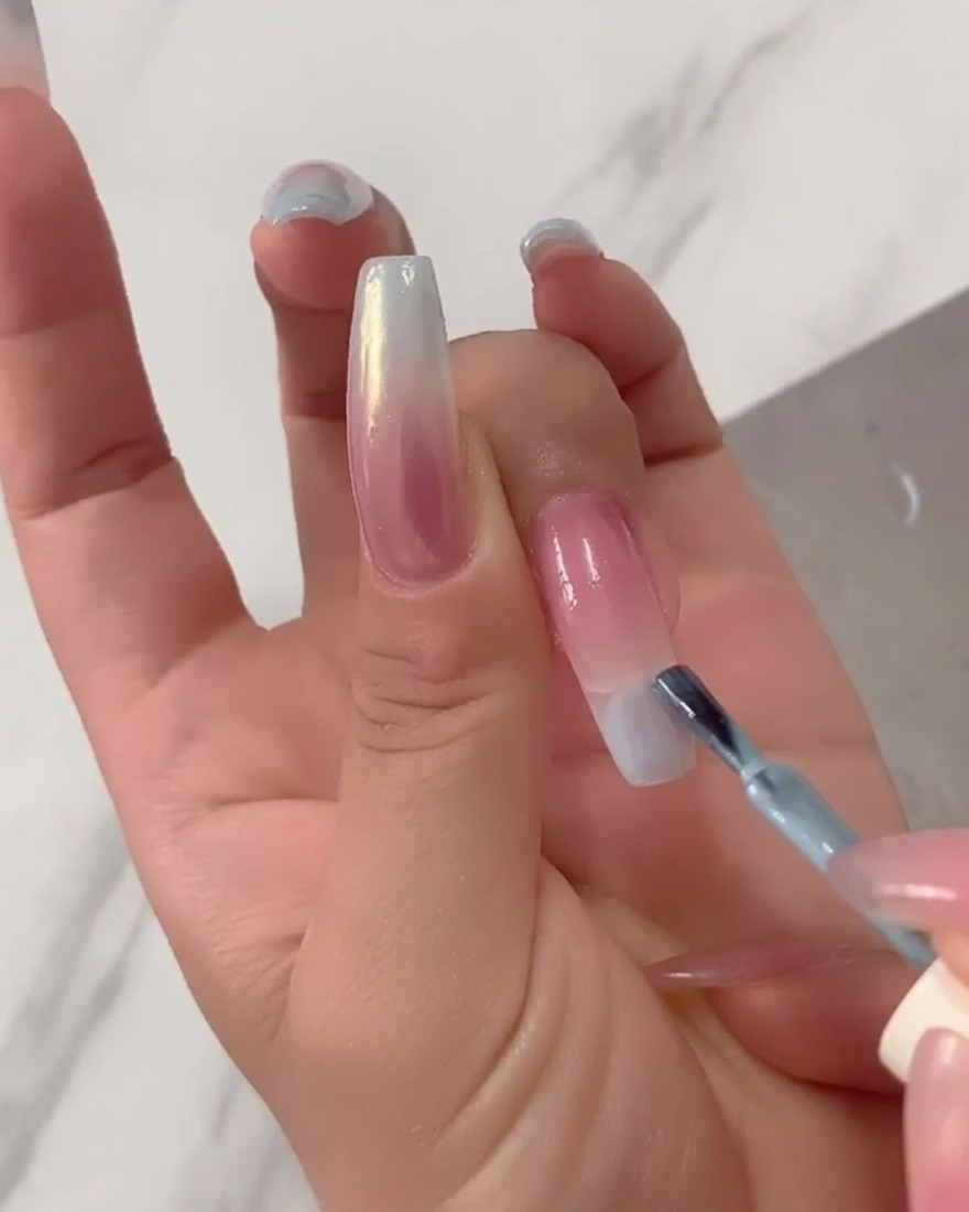 Gros plan dun pinceau appliquant du vernis gel bleu clair non dilué directement sur la pointe dune longue extension dongle.