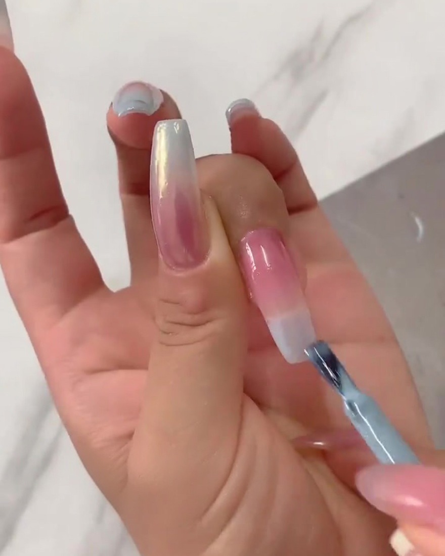 Gros plan dun pinceau plat estompant du vernis gel bleu concentré vers le bas depuis la pointe de longle sur une base nude rosée.