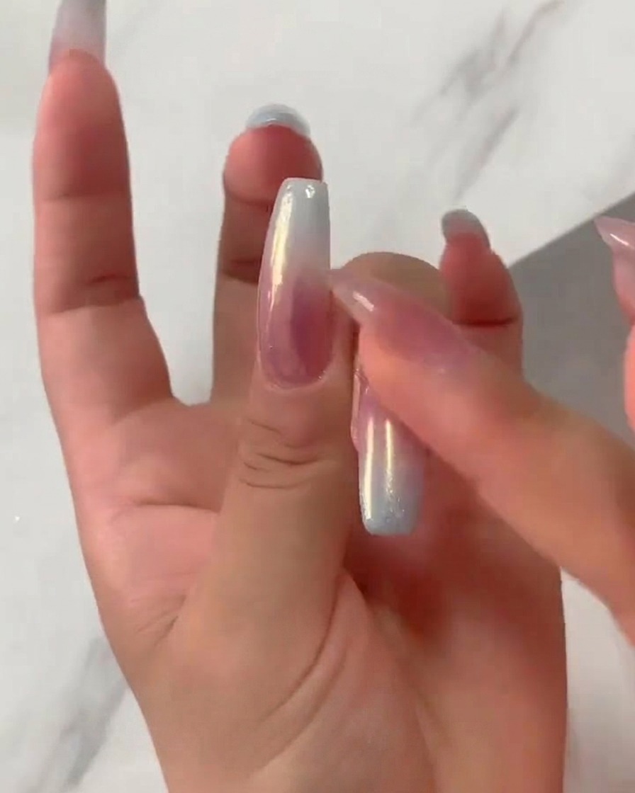 Un bout de doigt frottant fermement de la poudre chrome aurora irisée sur un ongle dégradé rose et bleu catalysé.