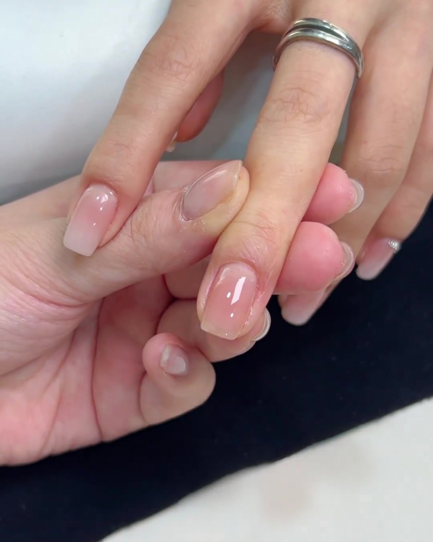 Un plan rapproché dun ongle carré recouvert dune couche lisse et brillante de vernis gel nude translucide appliquée uniformément.