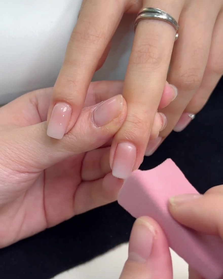 Une petite éponge rose tapotant du gel blanc sur le bout dun ongle pour créer un effet ombré.