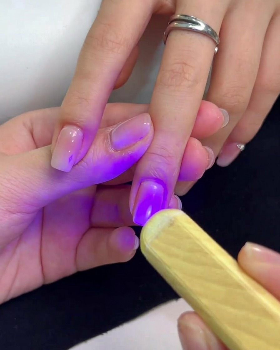 Une mini lampe UV portable émettant une lumière violette maintenue au-dessus dun ongle pour catalyser le vernis gel.