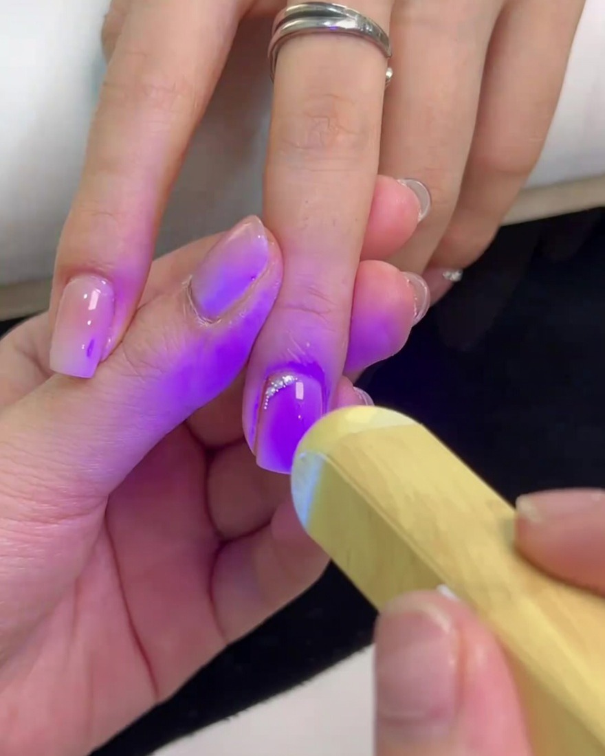 Une mini lampe UV portable diffusant une lumière violette sur un ongle carré pour catalyser la colle et fixer les cristaux.