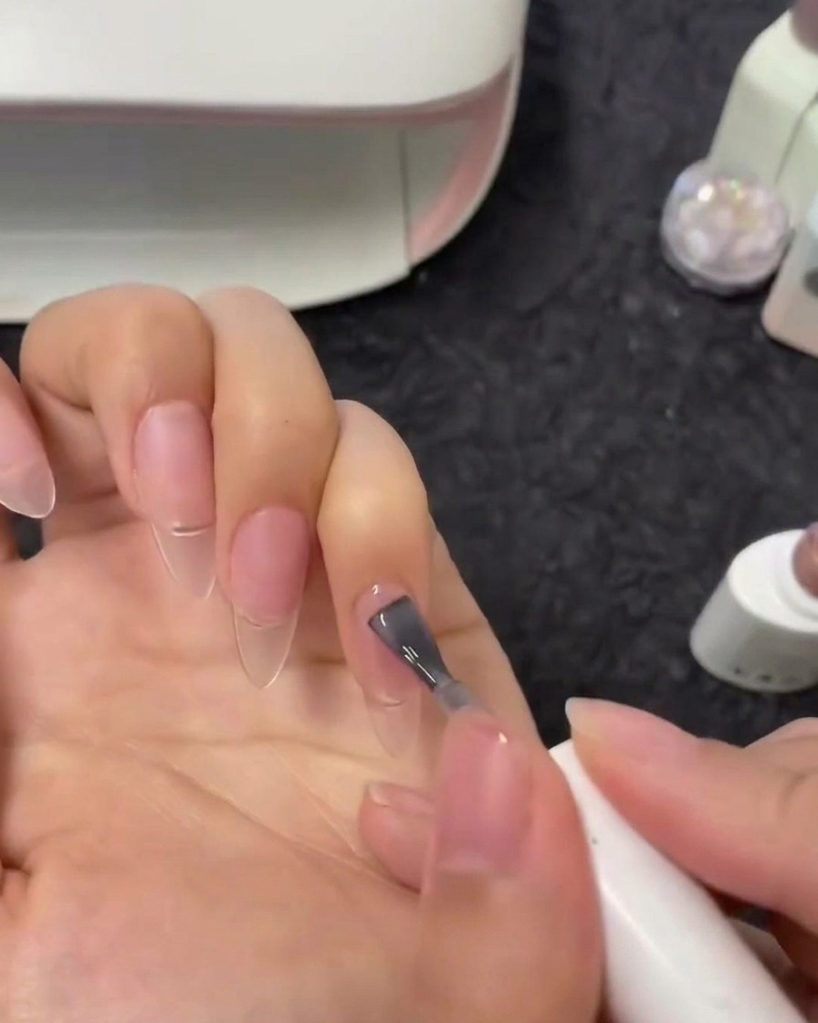 Vue rapprochée dun pinceau appliquant un vernis gel nude semi-transparent sur un ongle index.