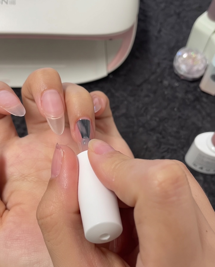 Vue rapprochée dun pinceau appliquant du vernis gel nude sur un ongle majeur.