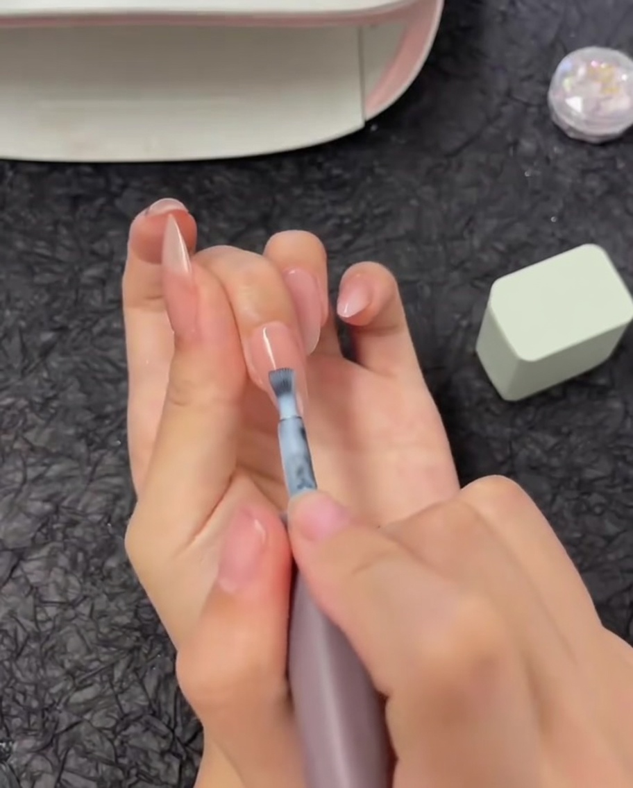 Un pinceau appliquant une bande horizontale de vernis gel blanc sur la moitié supérieure dun ongle.