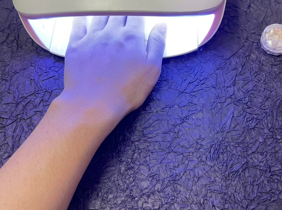 Une main reposant à lintérieur dune lampe UV/LED brillante pour catalyser le vernis gel, sur une surface texturée violette.