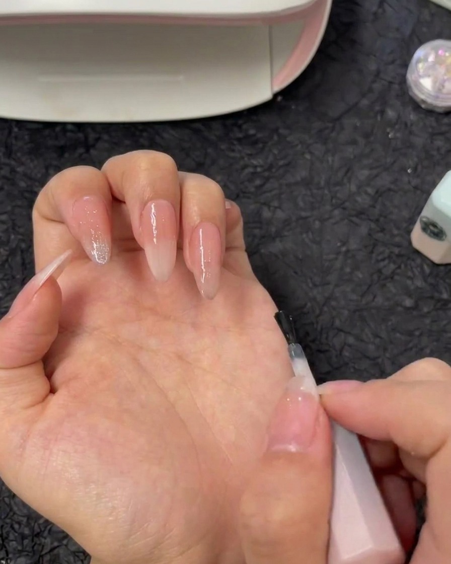 Un pinceau appliquant du gel de renforcement transparent directement sur un ongle index avec une base nude en dégradé.