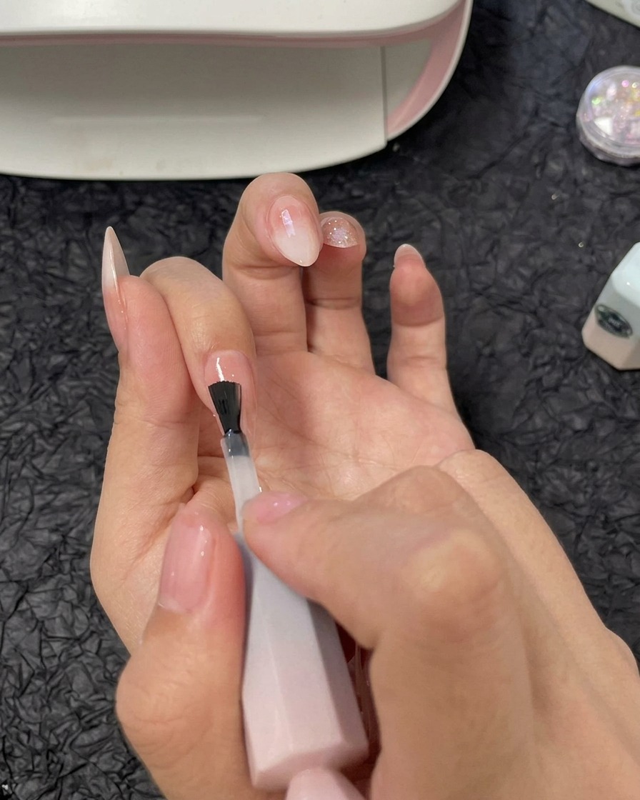 Une main appliquant une couche de gel de construction transparent sur longle de lannulaire avec un pinceau à vernis gel.