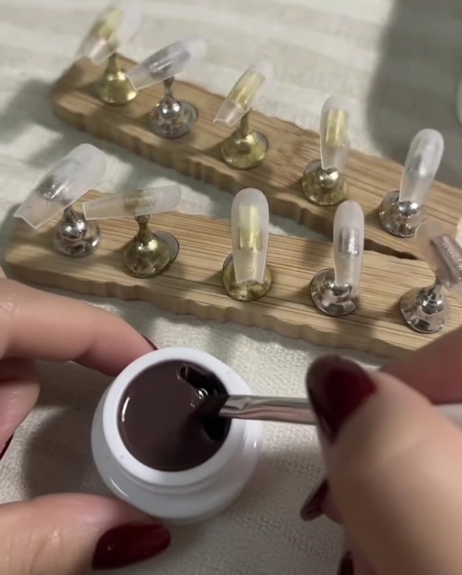 Un pinceau plat à gel trempant dans un petit pot contenant un vernis gel nude soutenu.