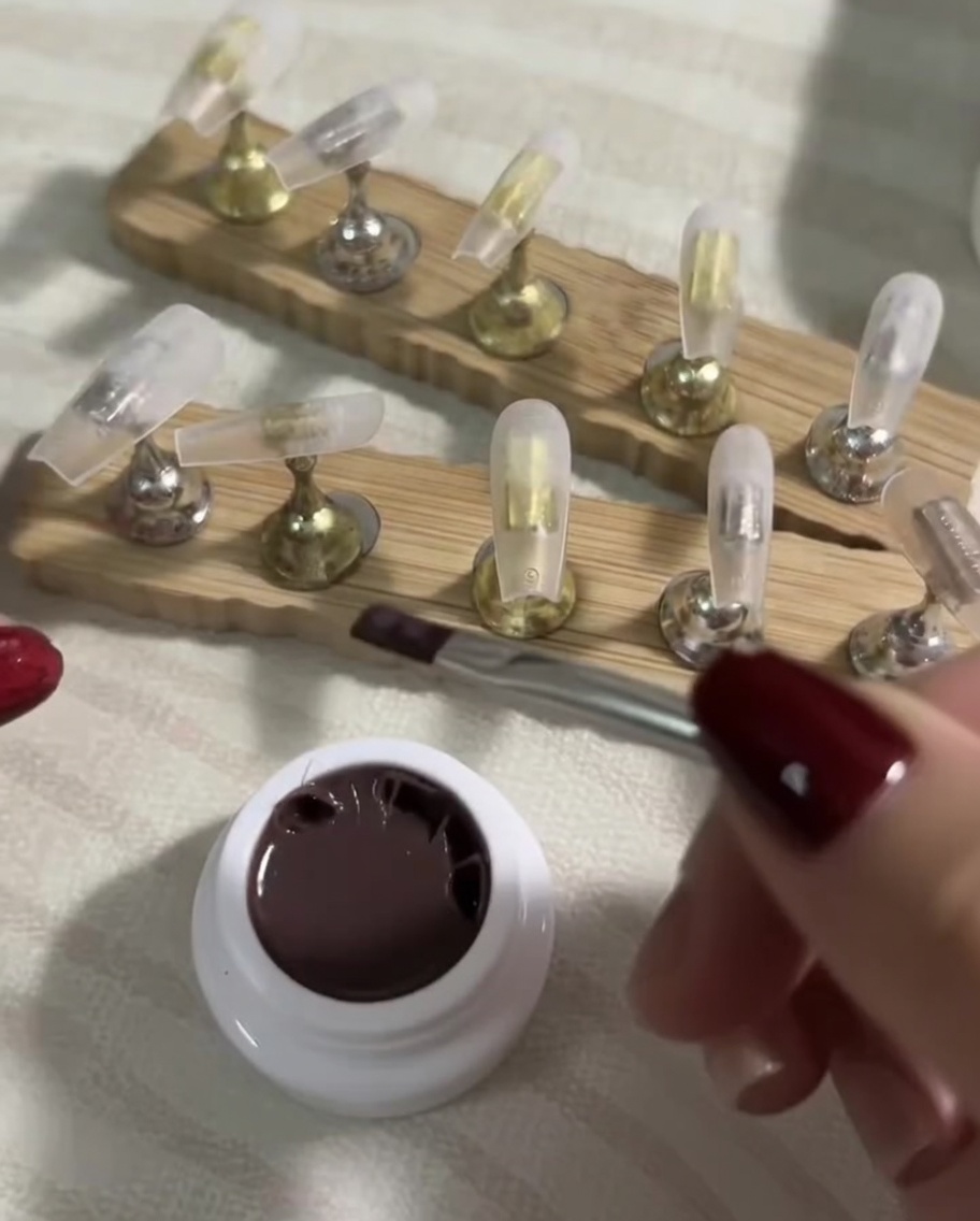Un pinceau plat appliquant en douceur une couche fine de vernis gel nude foncé sur un tip transparent.