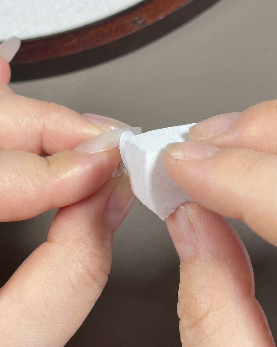 Une éponge à maquillage tamponnant du gel blanc sur la pointe dun ongle long en amande.