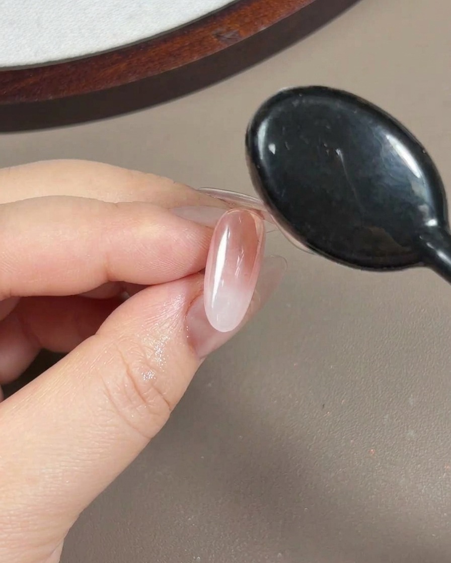 Vue rapprochée dun pinceau appliquant un gel de construction transparent et visqueux sur un ongle recouvert de poudre aurora.