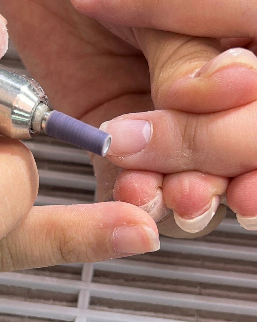 Ponceuse électrique avec un embout émeri violet lissant la plaque de longle près du repli de la cuticule.