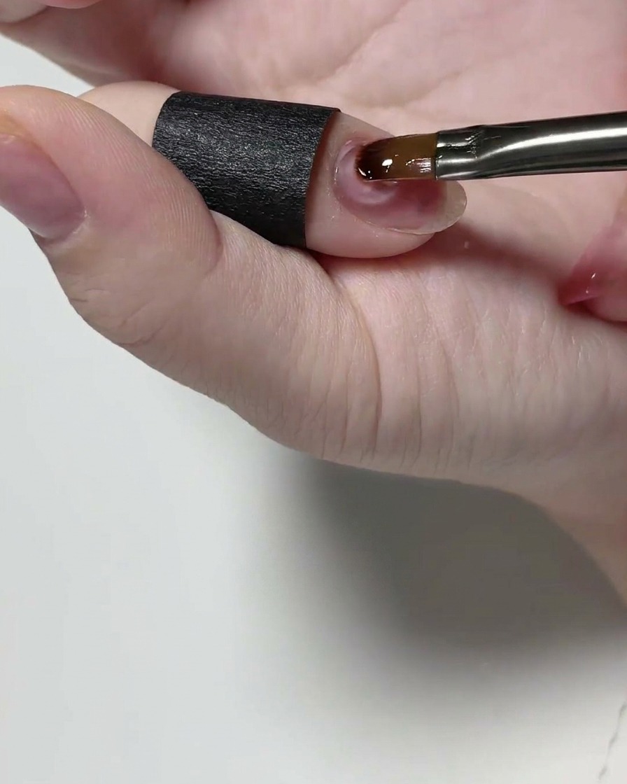 Un pinceau de détail appliquant un gel de construction transparent sur un ongle naturel.