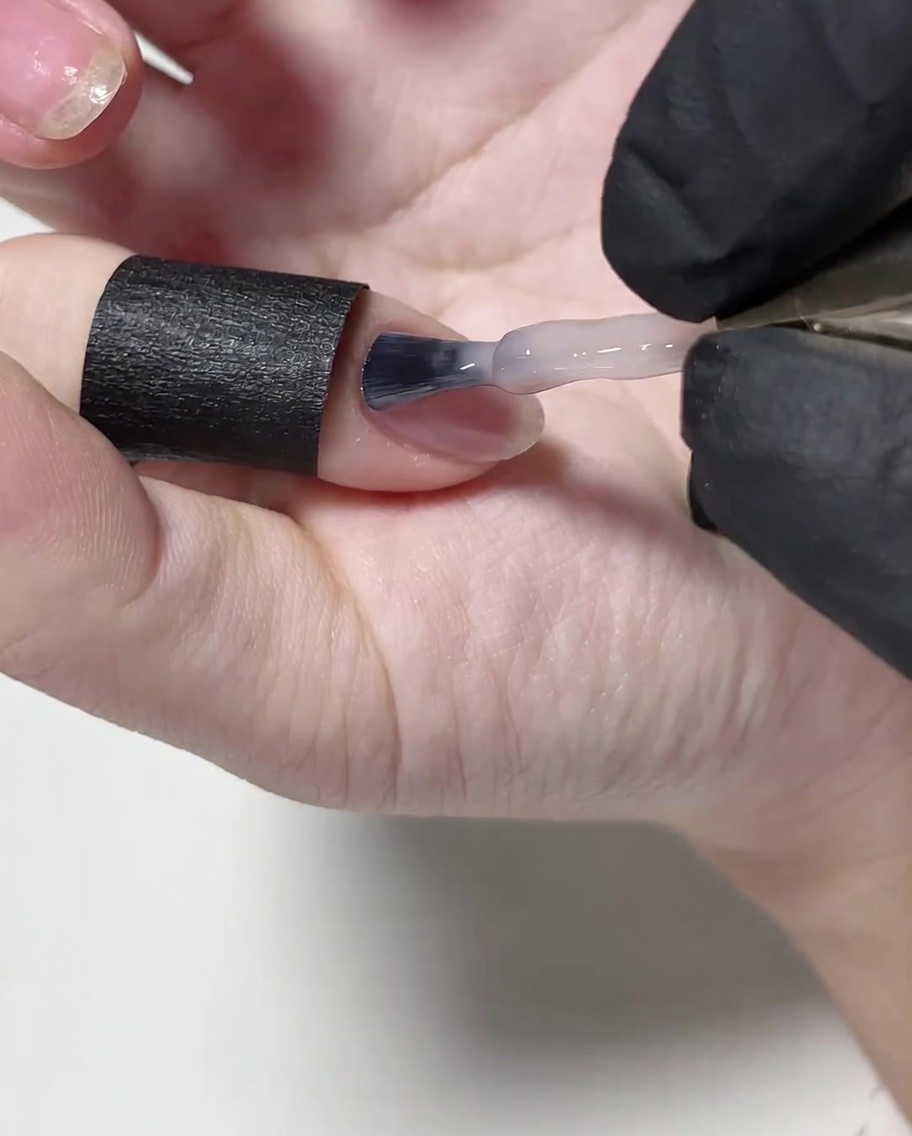 Un pinceau appliquant une fine couche de vernis gel nude sur la surface de longle.