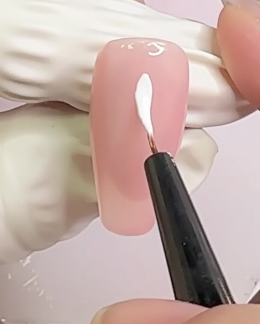 Un ongle nude avec deux lignes blanches croisées formant un motif en X au centre.