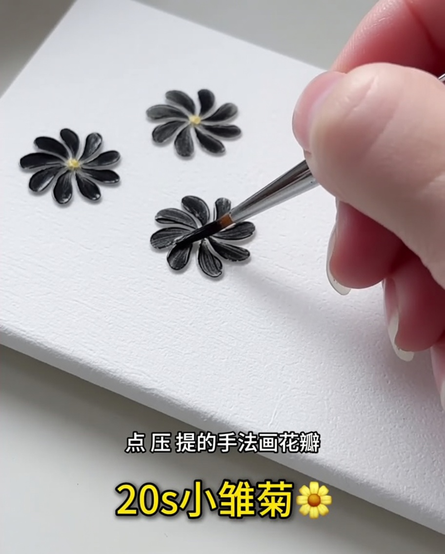 Gros plan sur un pinceau liner fin appliquant un pétale en gel noir sur une surface blanche.