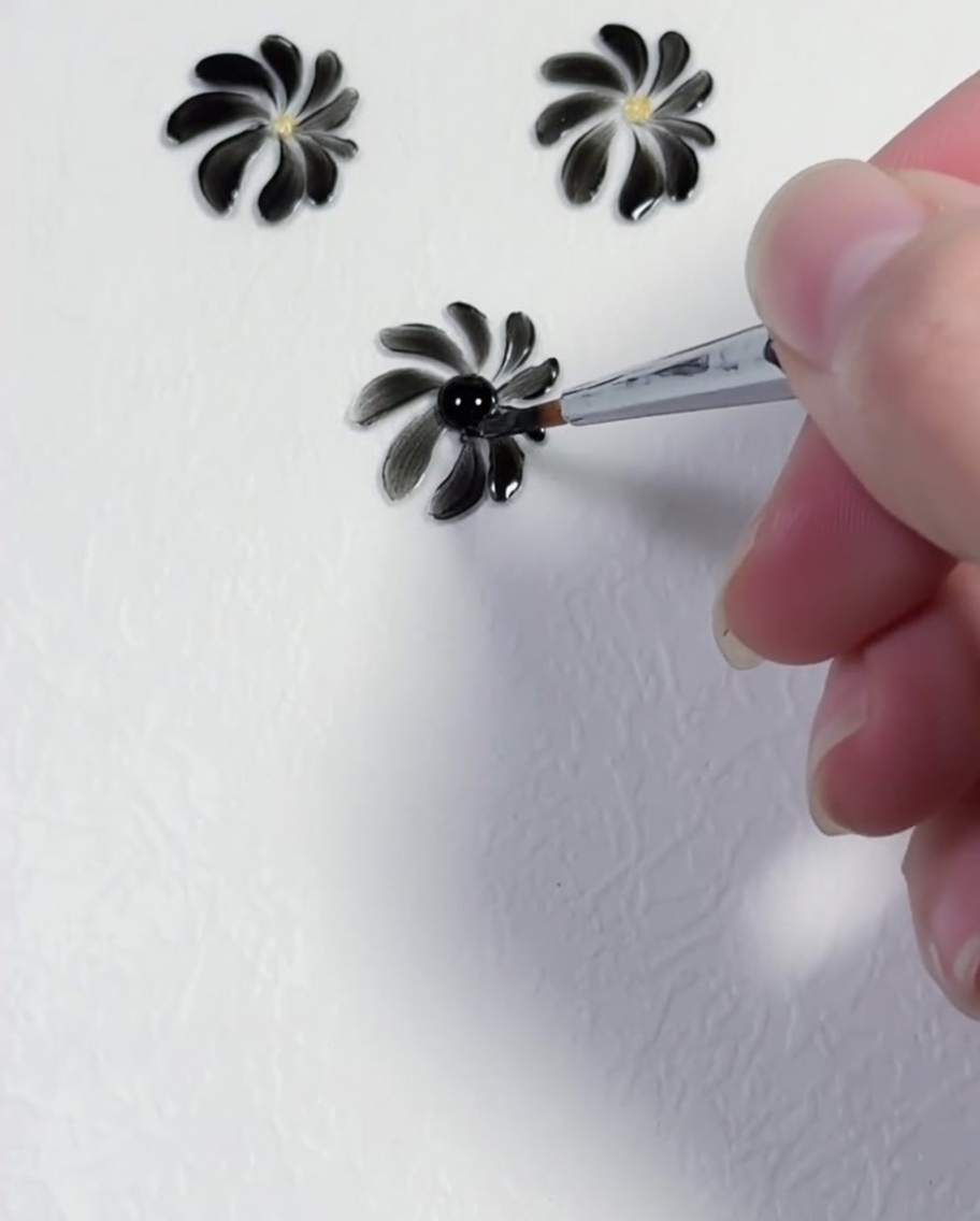 Un dotting tool déposant un point jaune précis au centre dun design de marguerite noire.