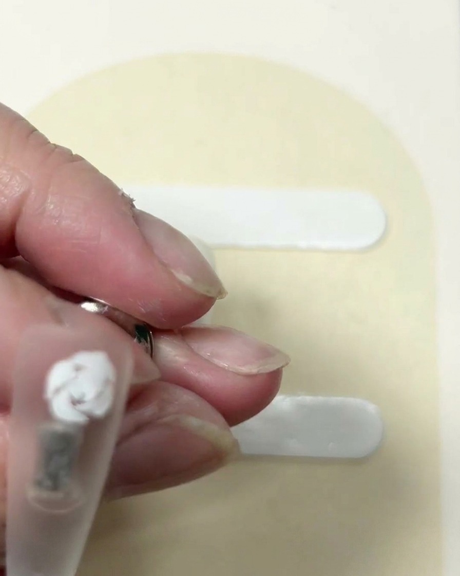 Vue rapprochée dune rose blanche partiellement formée sur un ongle, avec des traits courbes distincts définissant les couches extérieures.