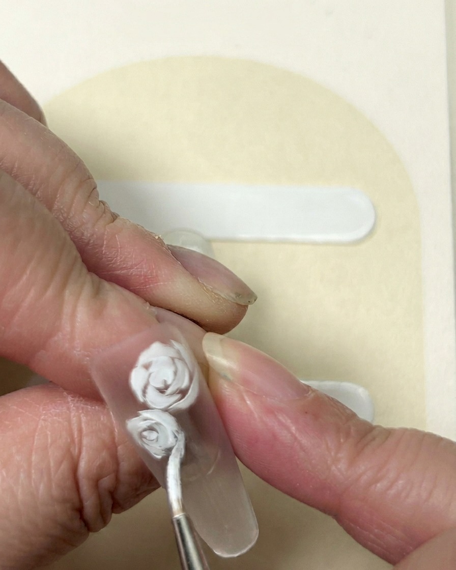Gros plan sur une fleur à cinq pétales peinte en gel blanc à côté dun design de rose établi.