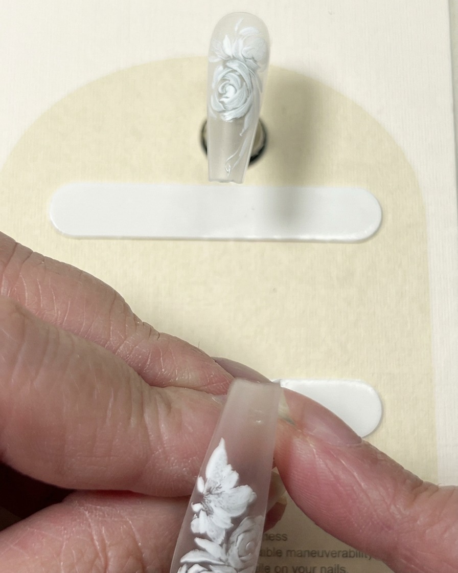 Vue rapprochée dun pinceau ajoutant des lignes de détail blanches fines au centre et sur les pétales dun design floral peint sur un ongle.