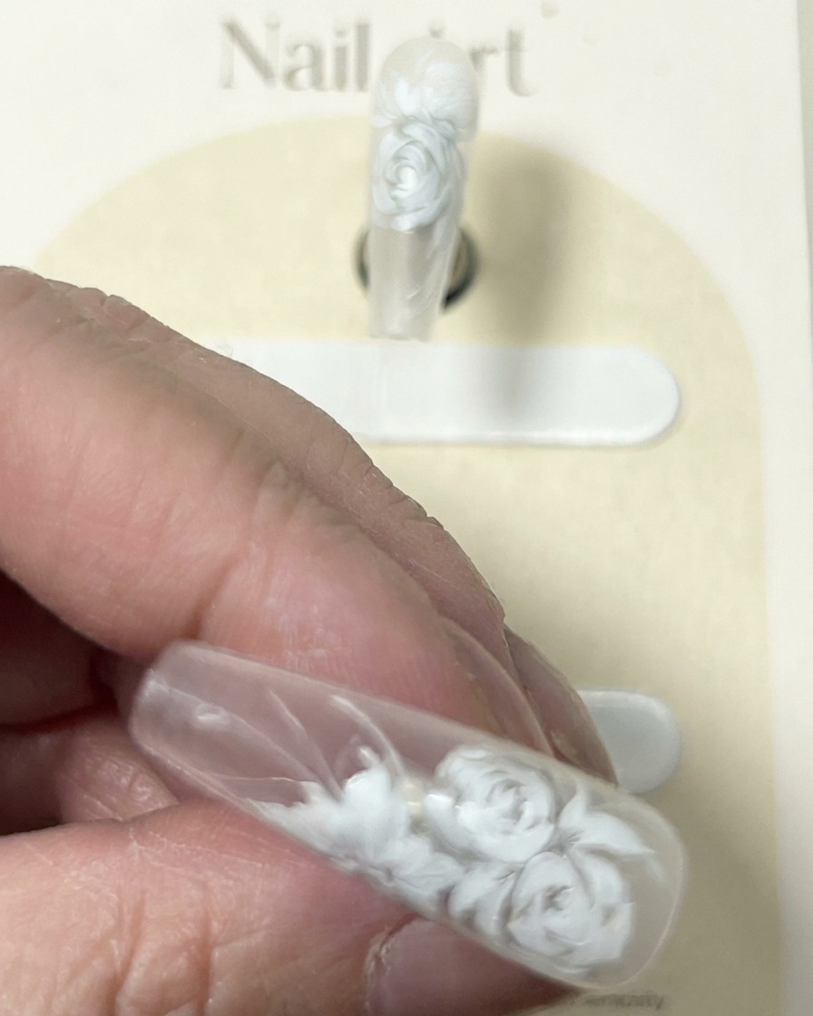 Gros plan sur un ongle avec un design détaillé de rose blanche, montrant le pinceau ajoutant des reflets blancs délicats finaux.