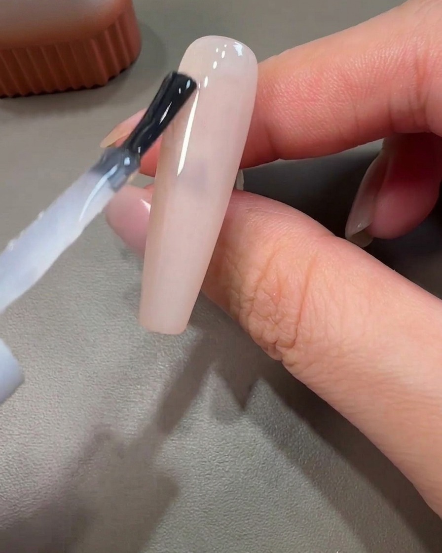 Gros plan dun pinceau liner appliquant du gel rose dans un mouvement circulaire sur une base non catalysée.