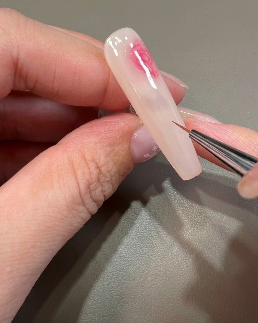 Un pinceau fin travaillant les détails dun motif de fleur rose aux contours doux sur longle.