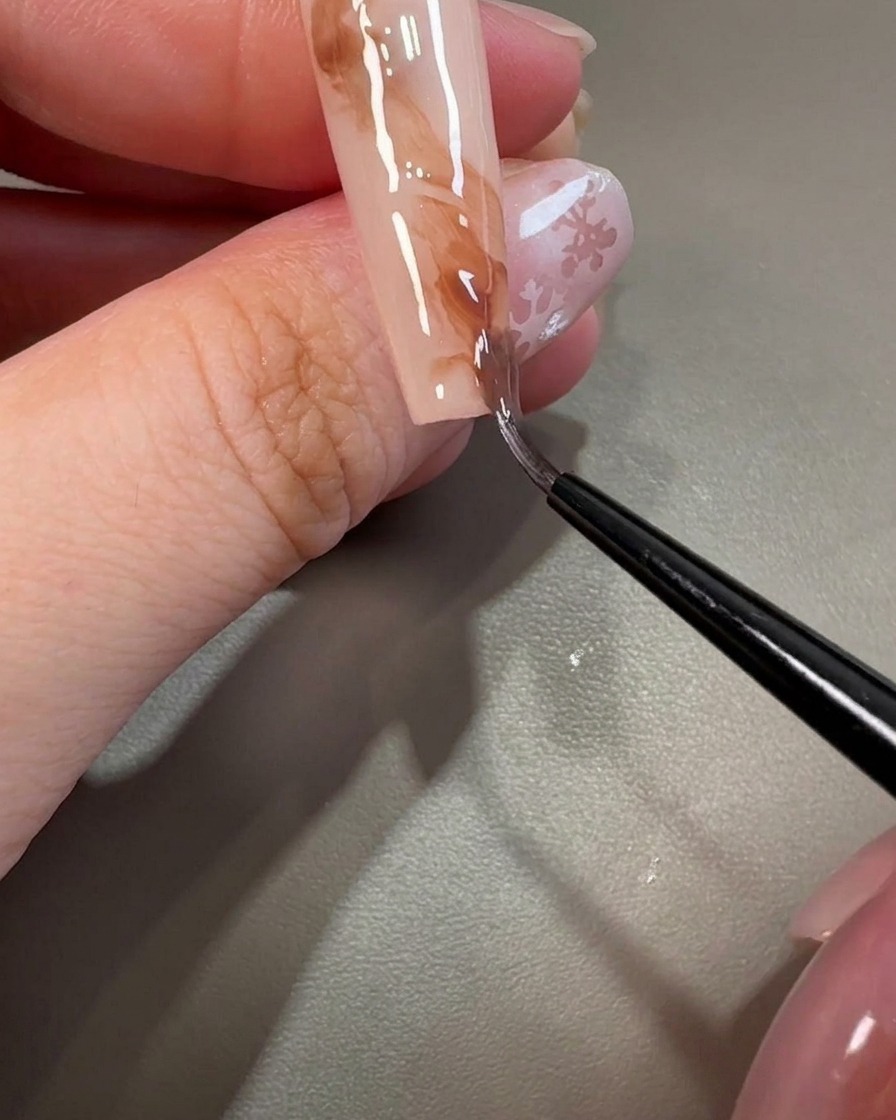 Un pinceau liner tirant à travers le gel marron pour créer des textures marbrées tourbillonnantes sur longle.