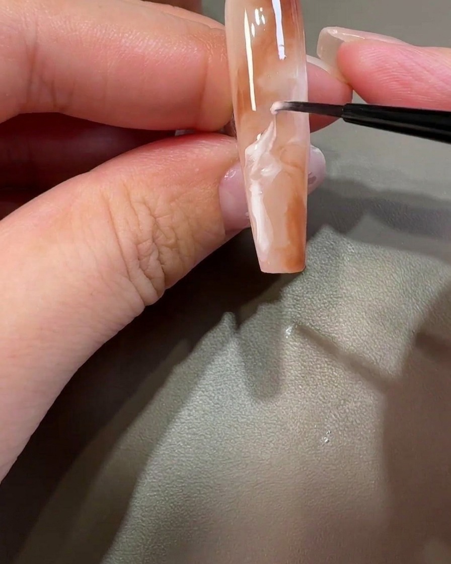 Un pinceau liner tirant du gel blanc à travers le design marron pour créer des motifs marbrés tourbillonnants.