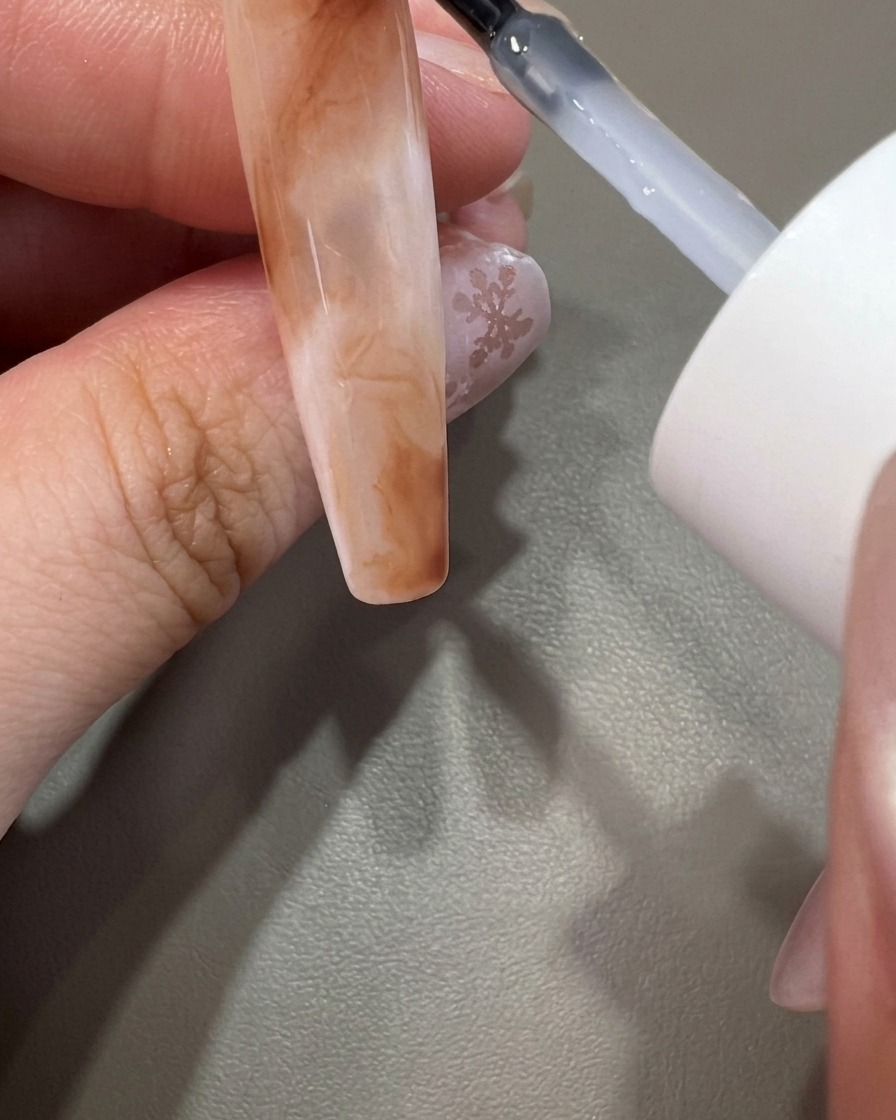 Un pinceau appliquant un top coat transparent sur un design dongle marbré terminé.