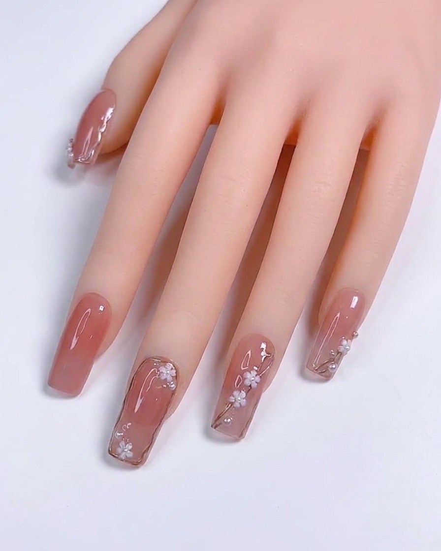 Gros plan sur un pinceau de détail appliquant de fines lignes métalliques argentées sur un ongle en gel nude.