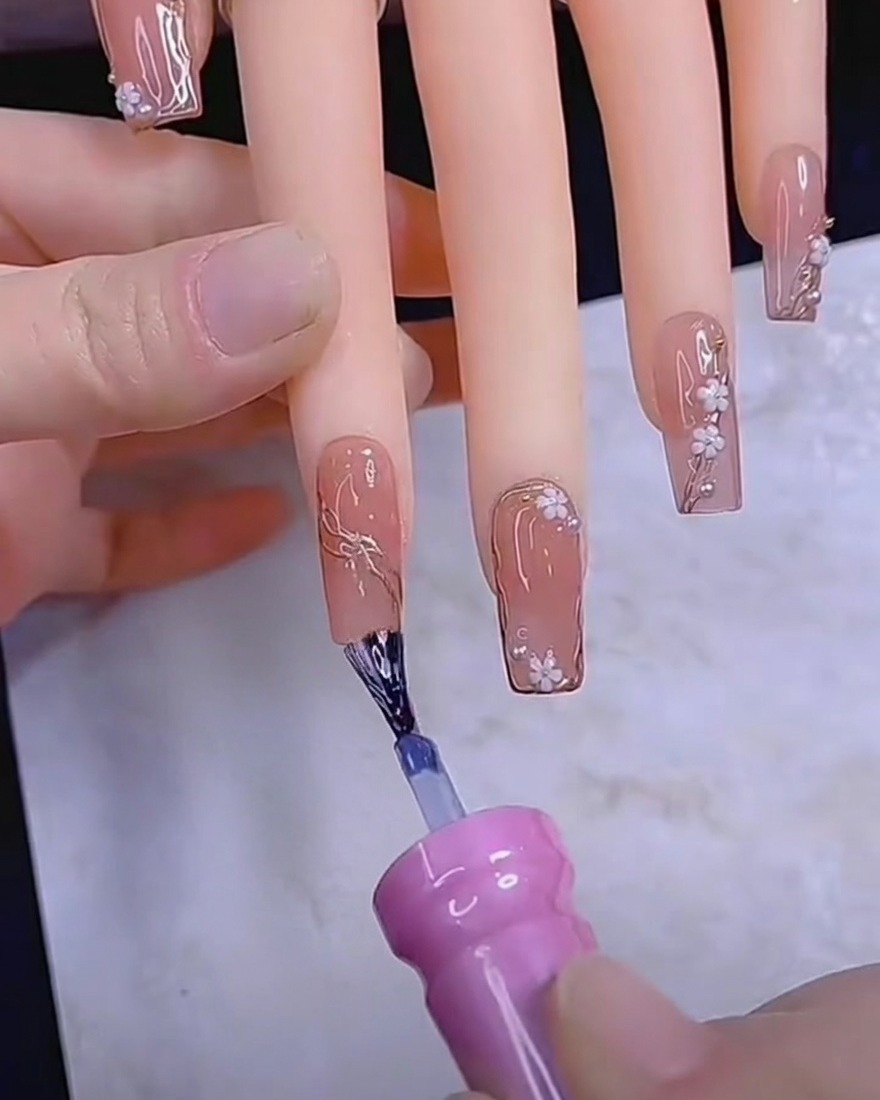 Un outil de type dotting tool plaçant de petits pétales de fleurs blancs sur un ongle en gel.