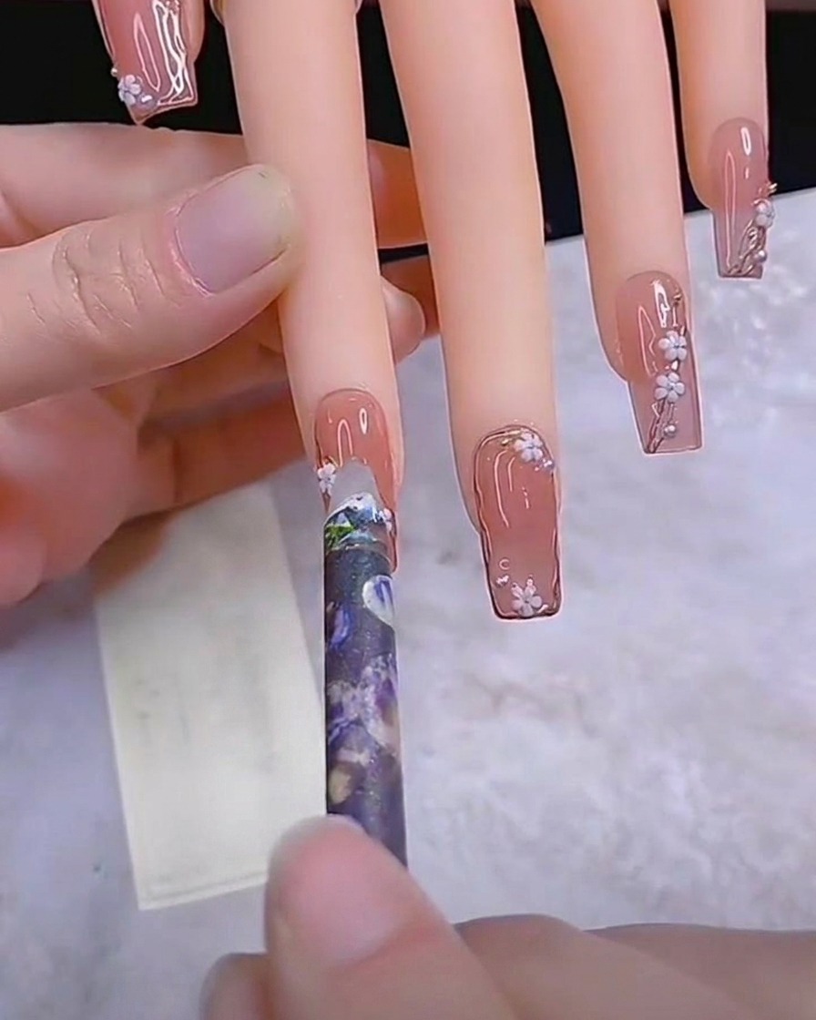 Un pinceau liner fin peignant de fines tiges sur un ongle.