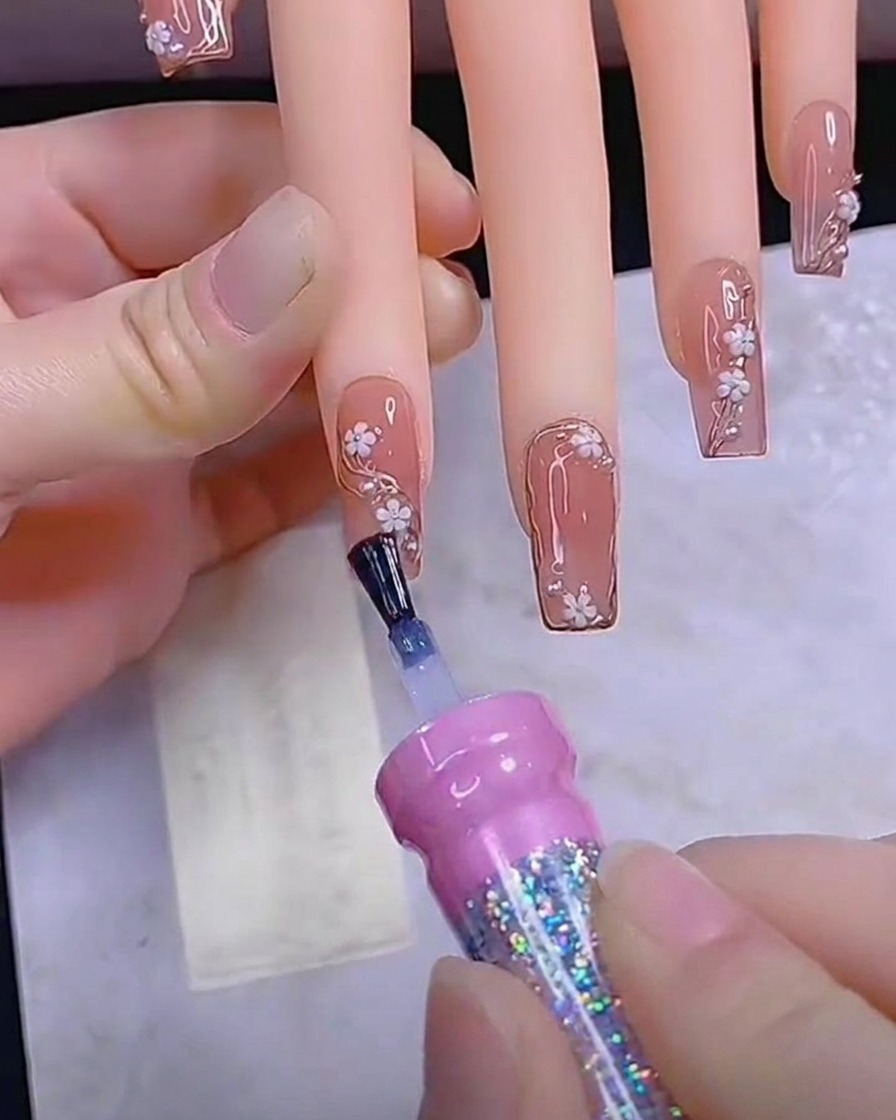 Un pinceau appliquant une dernière couche de top coat brillant sur un ongle entièrement décoré.