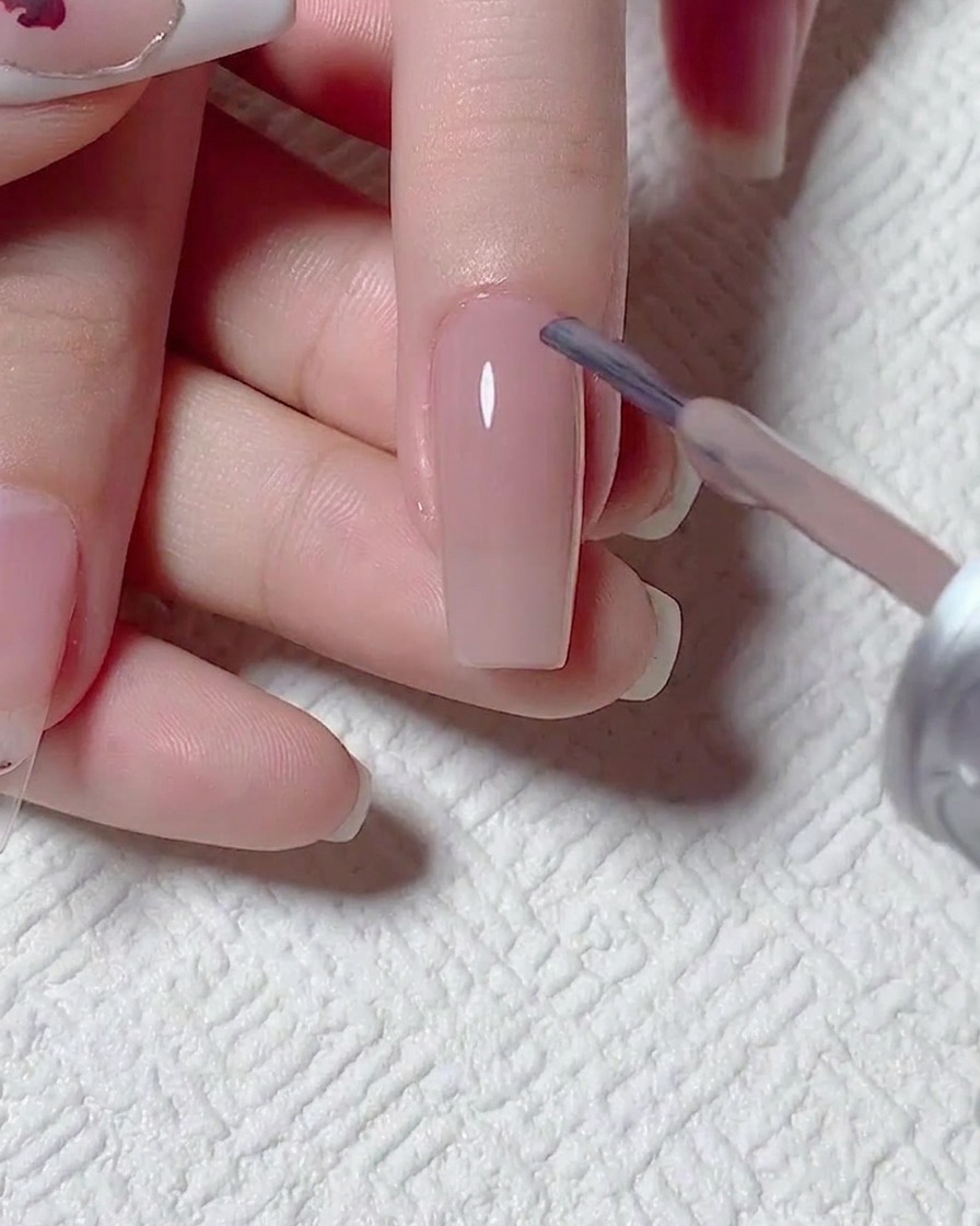 Gros plan dun pinceau appliquant un vernis gel nude transparent sur la surface de longle préparé.