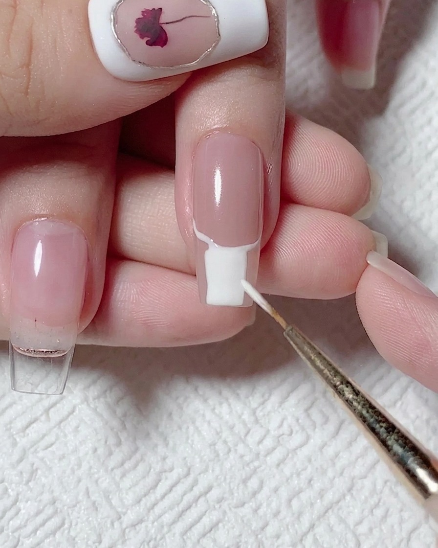 Un pinceau plat remplissant la partie inférieure de longle avec du vernis gel blanc opaque.