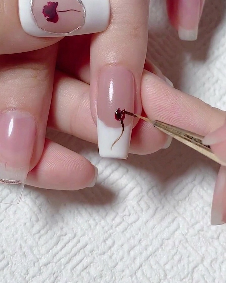 Gros plan dun pinceau de précision ajoutant du relief au design de rose avec du vernis gel rouge.