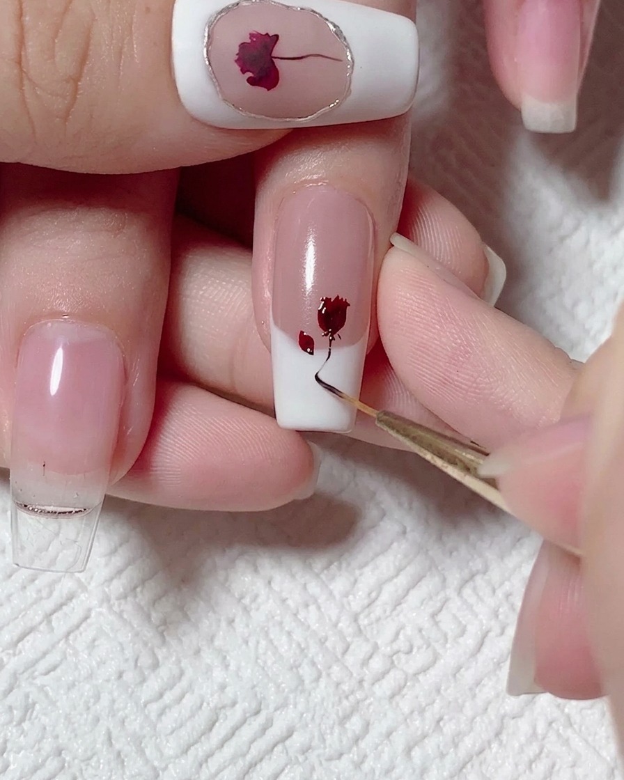 Un pinceau liner tirant une ligne fine de gel noir-brun vers le bas depuis une rose peinte en rouge sur un ongle.