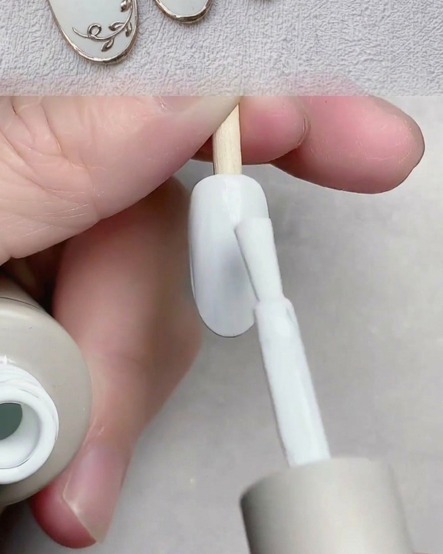Un pinceau appliquant un vernis gel blanc lisse sur une capsule dongle.