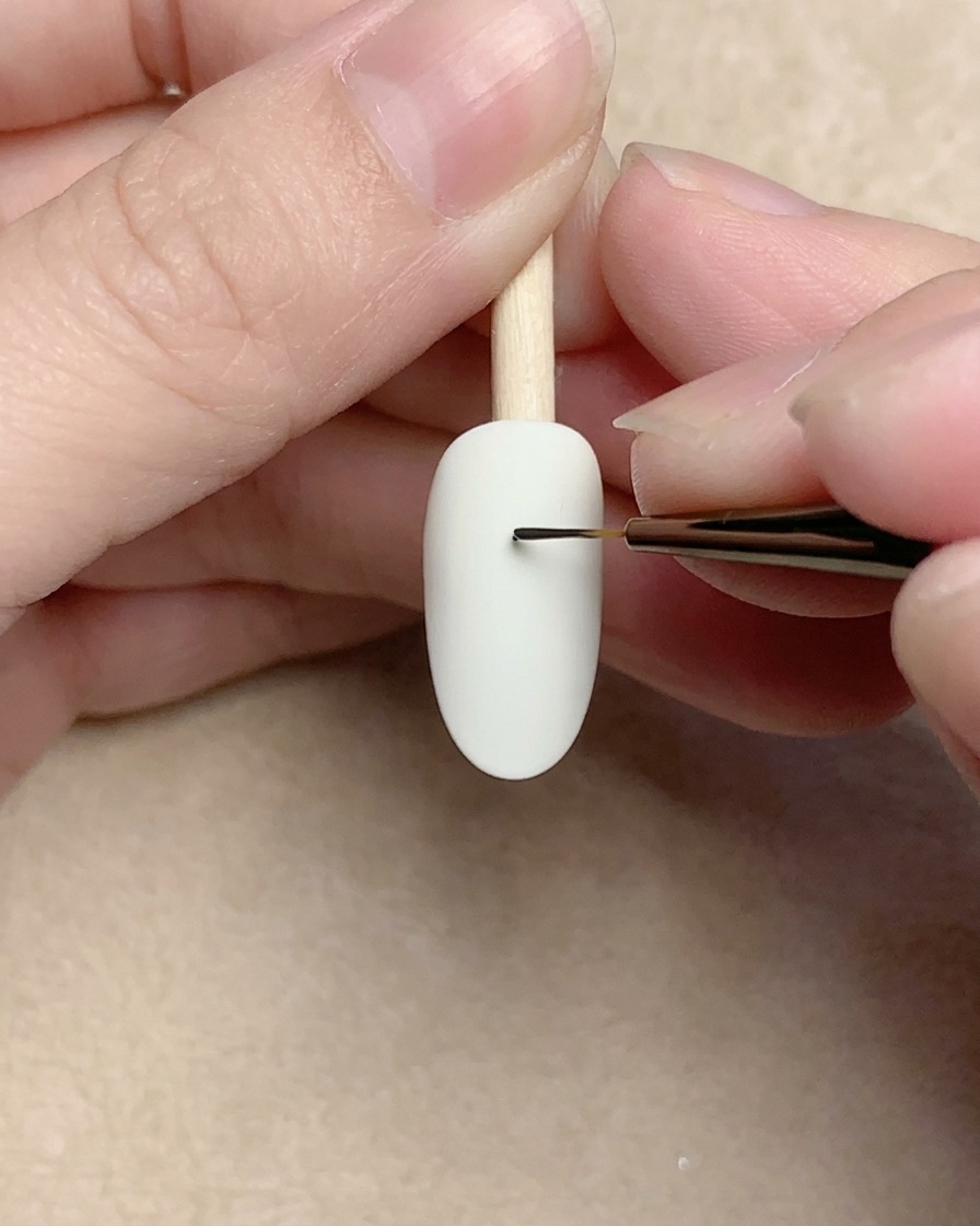 Gros plan dun pinceau liner dessinant une minuscule spirale noire sur un ongle blanc.